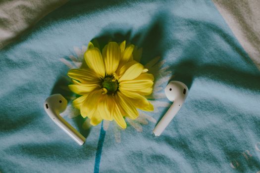 Close-up of a yellow flower and wireless earbuds on a blue fabric, creating a delicate still life.