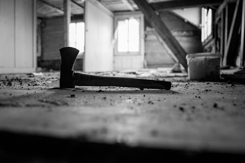Grayscale Photo of a Wooden Axe on the Floor of an Abandoned House