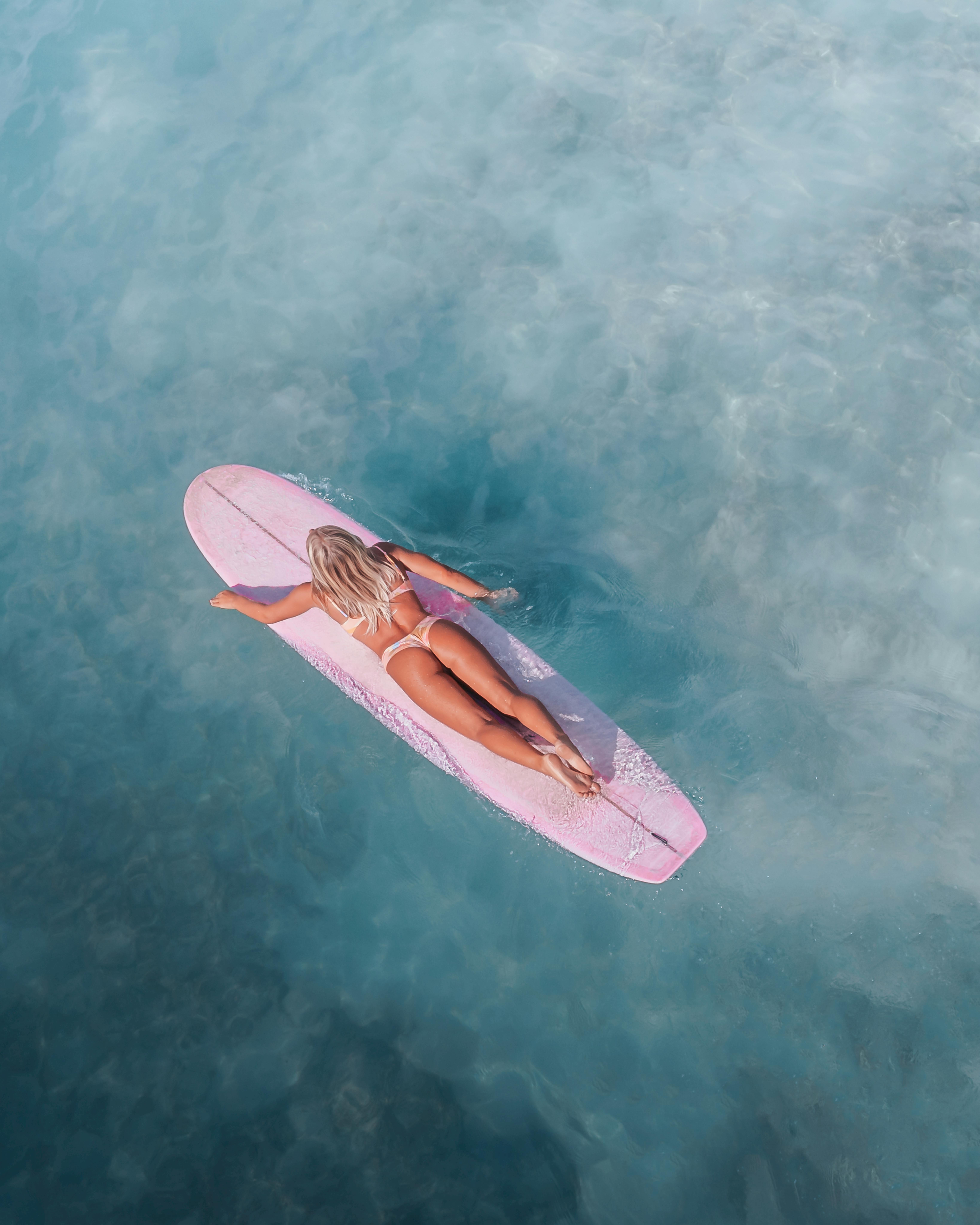 一个女人在清澈的蓝色水上的粉红色冲浪板上冲浪的头顶镜头，散发出冒险和自由的感觉