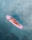 一个女人在清澈的蓝色水上的粉红色冲浪板上冲浪的头顶镜头，散发出冒险和自由的感觉