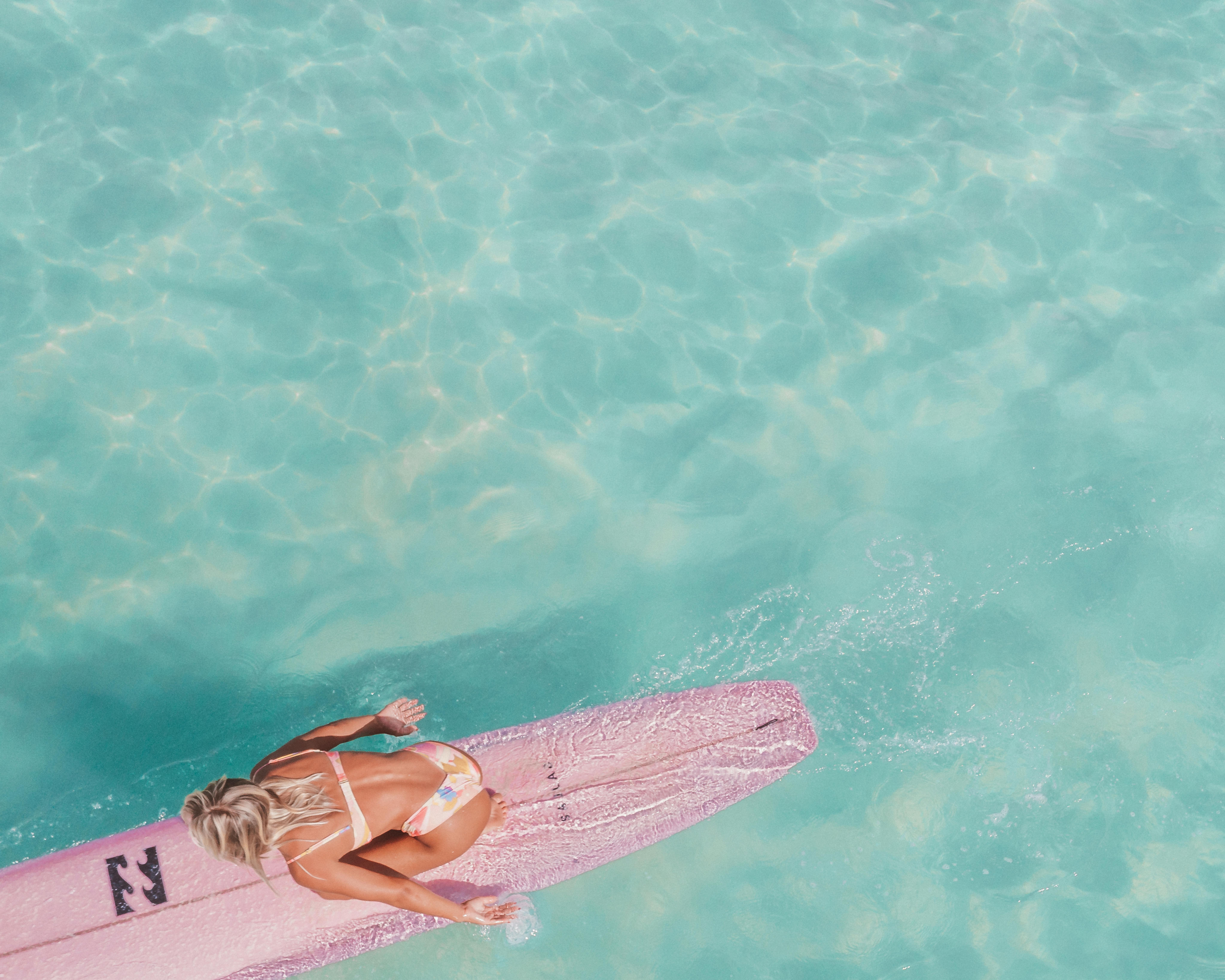 一个女人在粉红色的冲浪板上的透明绿松石水中的头顶镜头，包裹着夏天的共鸣