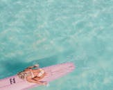 一个女人在粉红色的冲浪板上的透明绿松石水中的头顶镜头，包裹着夏天的共鸣