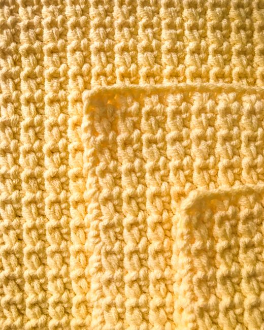 Detailed close-up of a yellow knitted fabric showing its intricate texture and pattern.