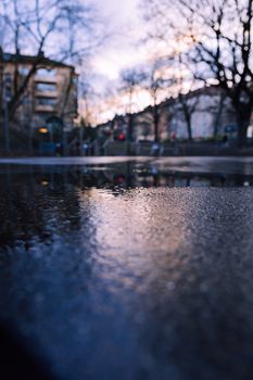 A cityscape reflection in a wet street creating a moody atmosphere during twilight.