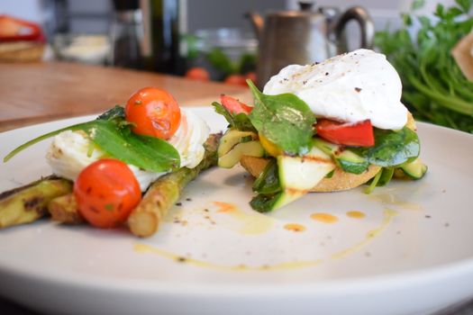 Close-up of a delicious breakfast with poached eggs, asparagus, and cherry tomatoes on a ceramic plate.