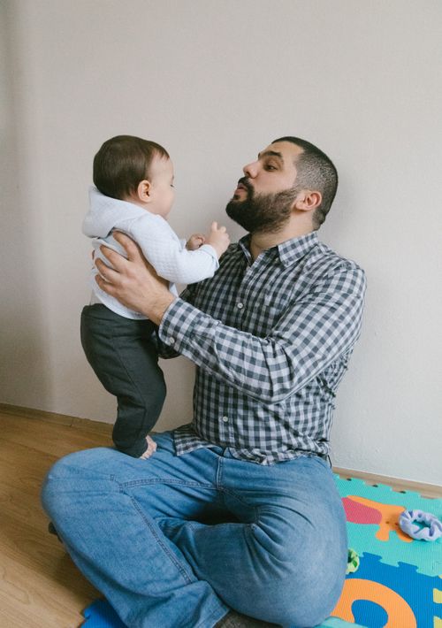 Free Caring father playing with infant son at home on a colorful play mat. Stock Photo