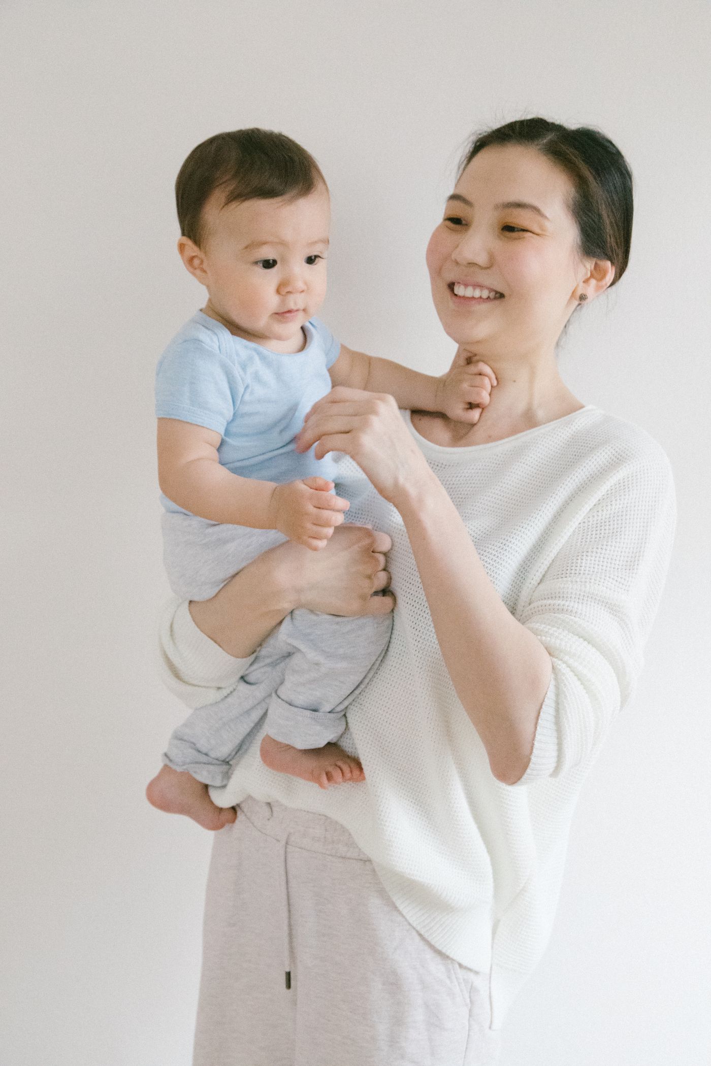 Jeune maman vêtue d’une chemise blanche portant son bébé dans un intérieur lumineux