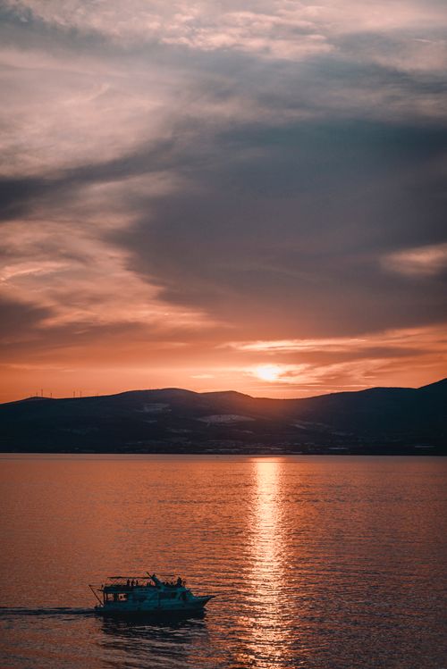 Free Boat sailing under a vibrant sunset sky on calm waters, capturing serene beauty. Stock Photo
