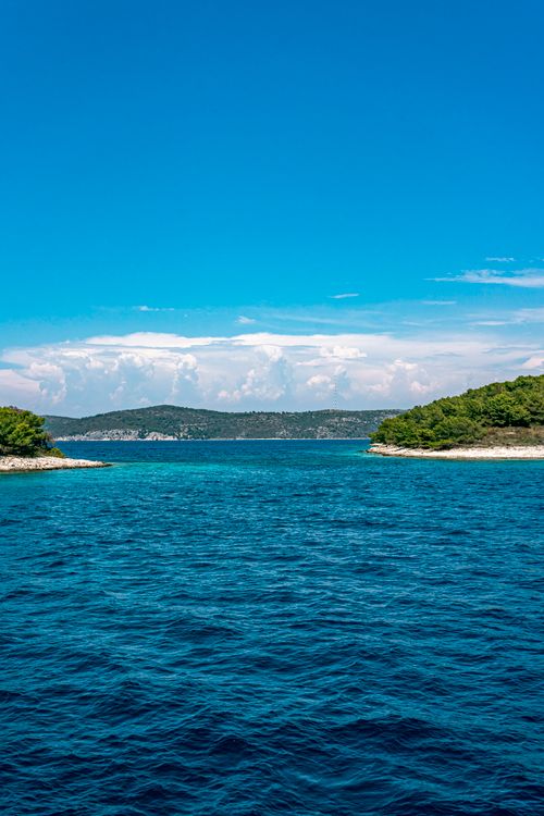 Free Peaceful coastal view with vibrant blue sea and lush green shoreline under a clear sky. Stock Photo