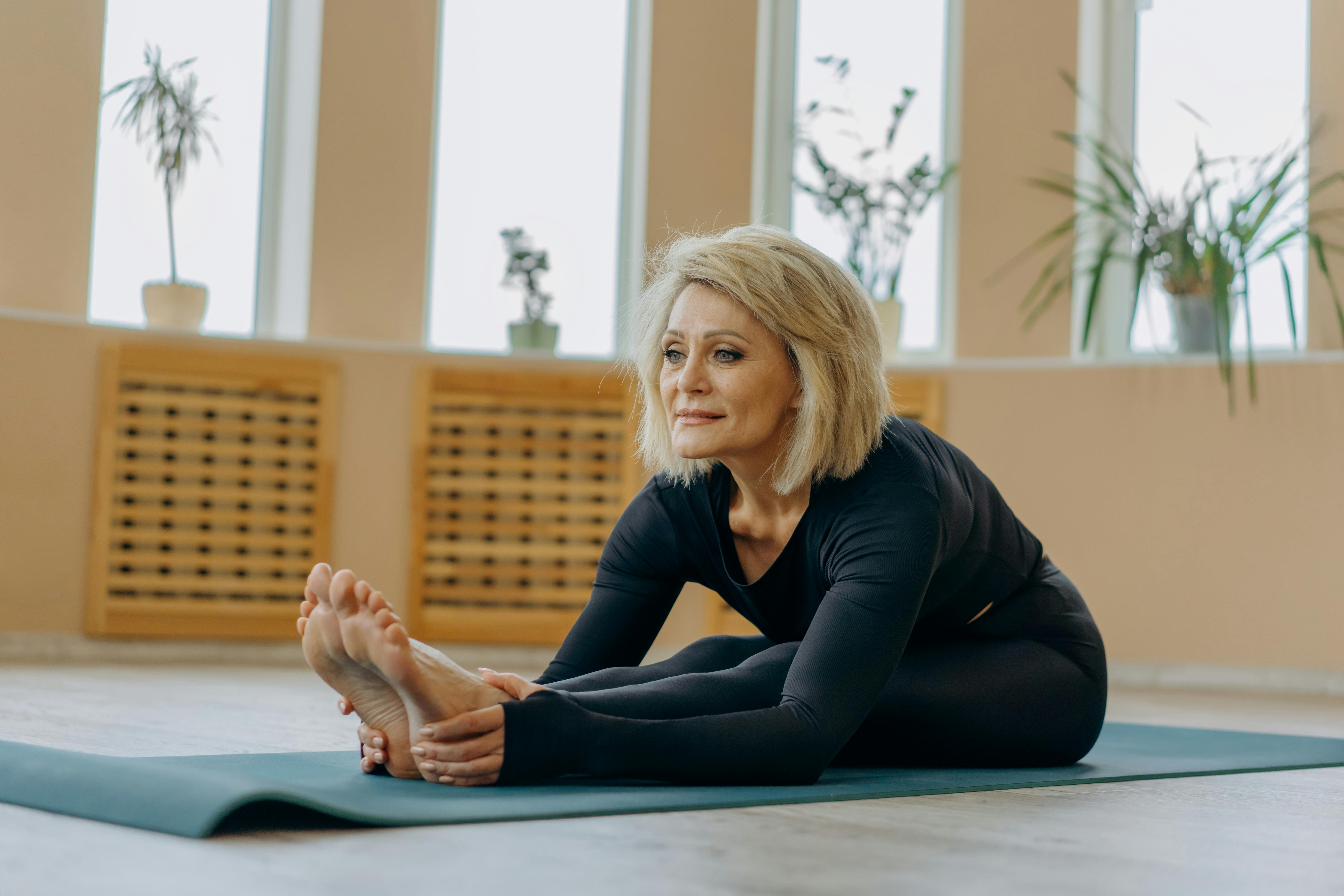 Elderly woman stretching on a yoga mat indoors, highlighting flexibility and wellness.