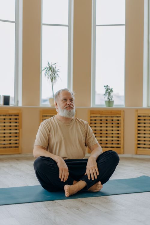 Free Elderly man with gray hair meditating on a yoga mat in a serene indoor setting. Stock Photo