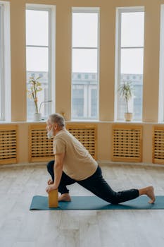 Elderly man exercising on a yoga mat indoors, using blocks for support.