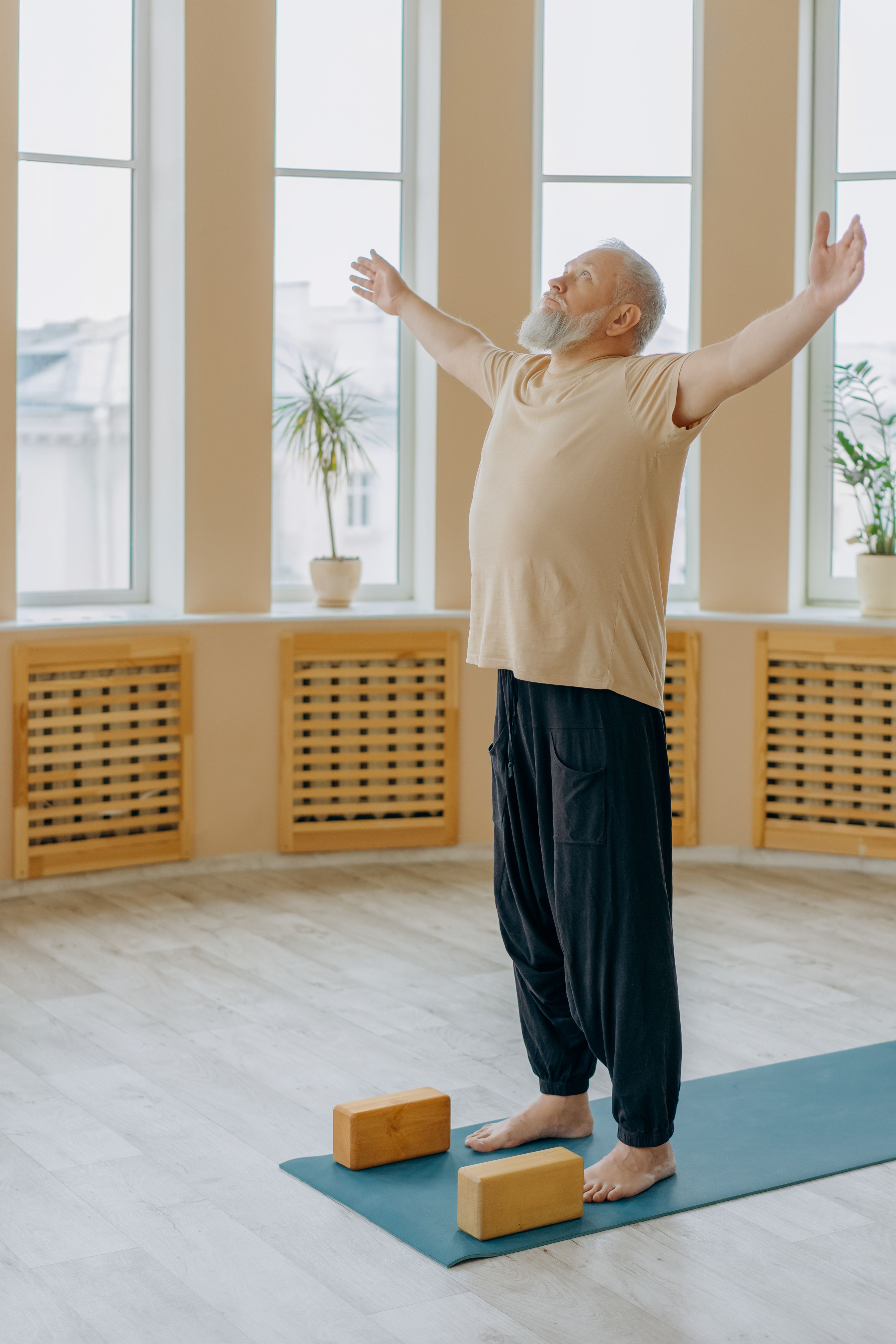 Elderly man performing a gentle standing stretch on a yoga mat