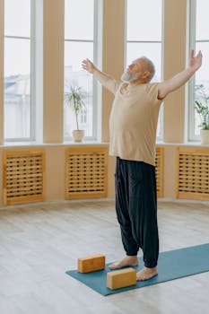 Elderly man performing yoga on a mat with blocks in a bright indoor setting.