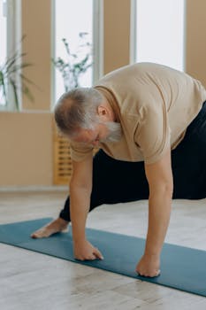 Elderly man in yoga pose on mat indoors, promoting healthy lifestyle.