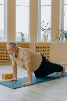 Elderly man performing yoga on a mat indoors for fitness and well-being.