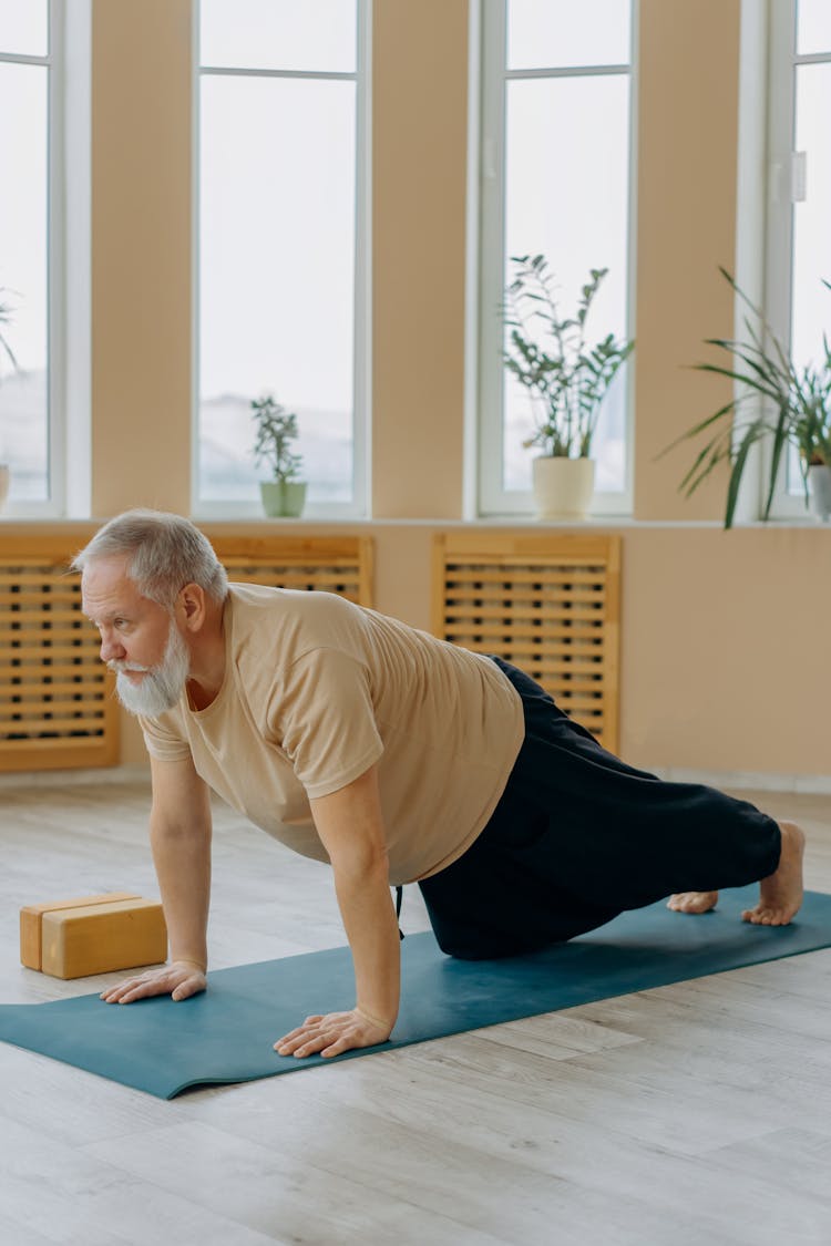 Man In Brown T-shirt And Black Pants Kneeling On A Yoga Mat