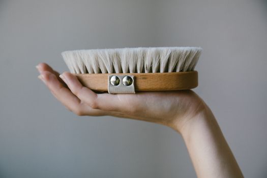 A detailed shot of a hand gracefully holding a natural bristle wooden brush with a strap.