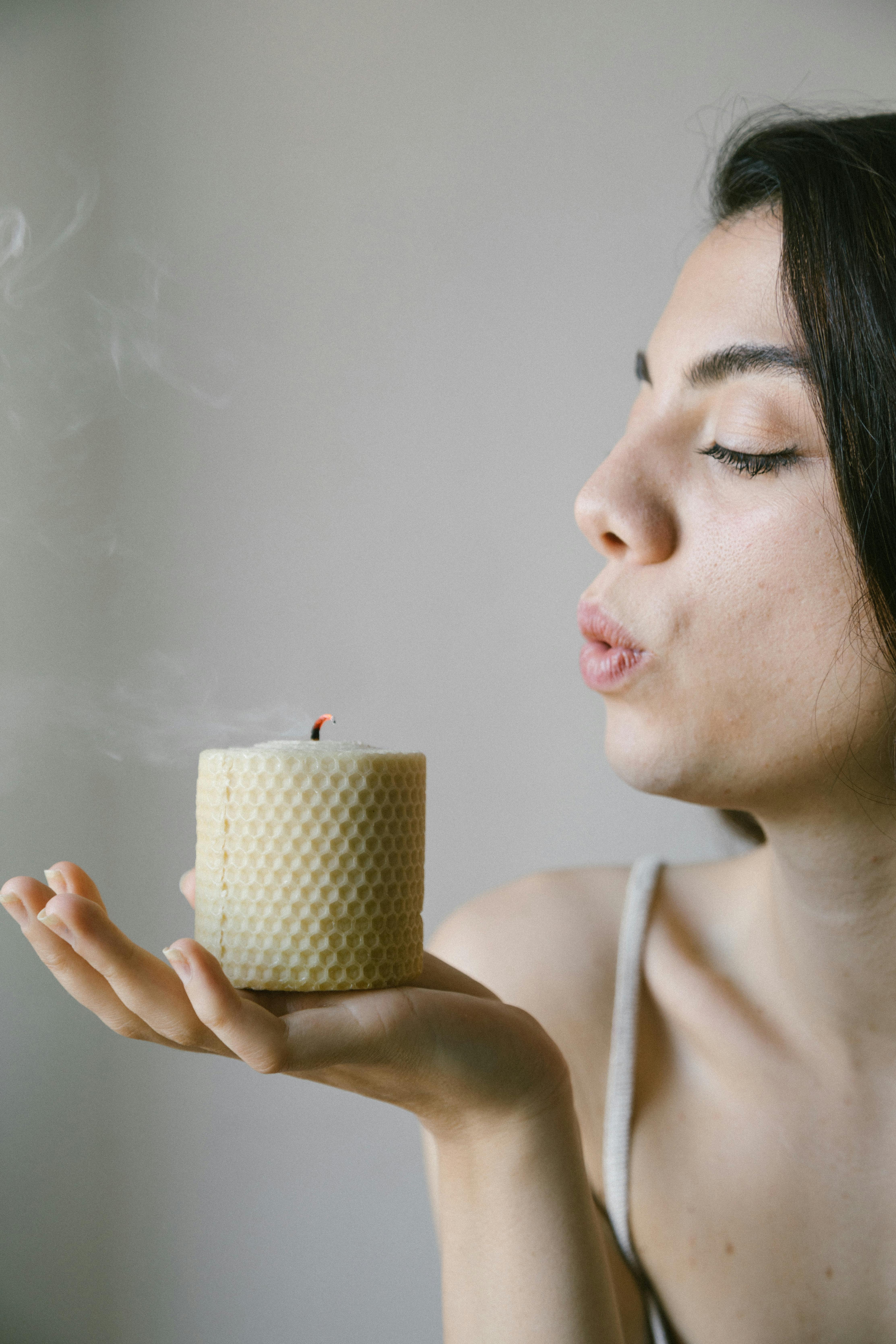 Close-up of a woman blowing out a natural, eco-friendly candle indoors, signifying sustainability.