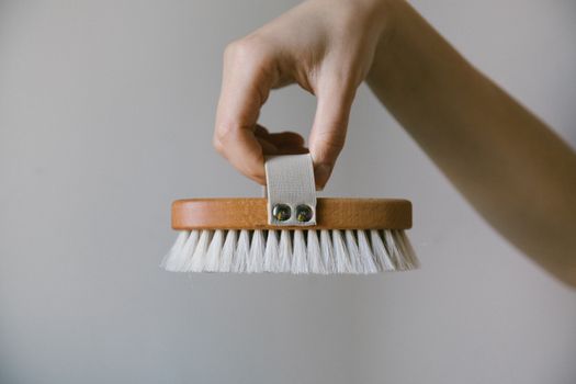 A hand holds a natural wooden shoe brush against a neutral background.