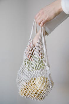 Close-up of a hand holding a reusable net bag filled with groceries.