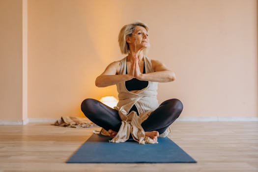 Full body of middle aged lady in activewear sitting on mat in lotus position in light room with closed eyes