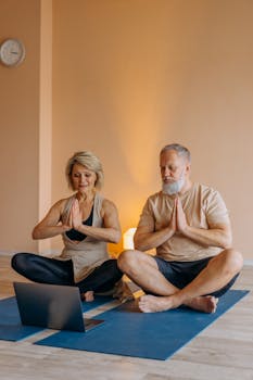 A senior couple meditating together on yoga mats while watching an online tutorial.