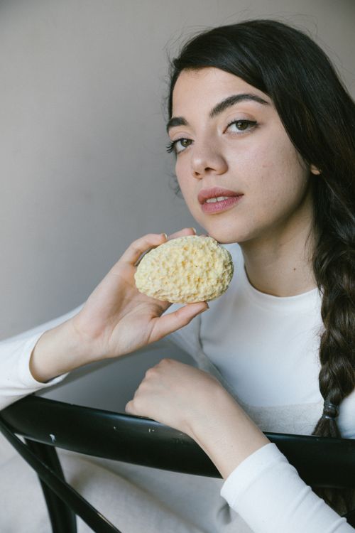 Free Young woman with a natural sponge, seated indoors, embodying a relaxed lifestyle. Stock Photo