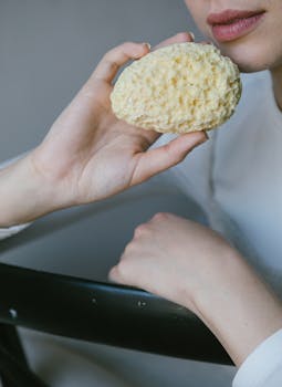 A natural sponge held by a woman's hand in a serene setting.