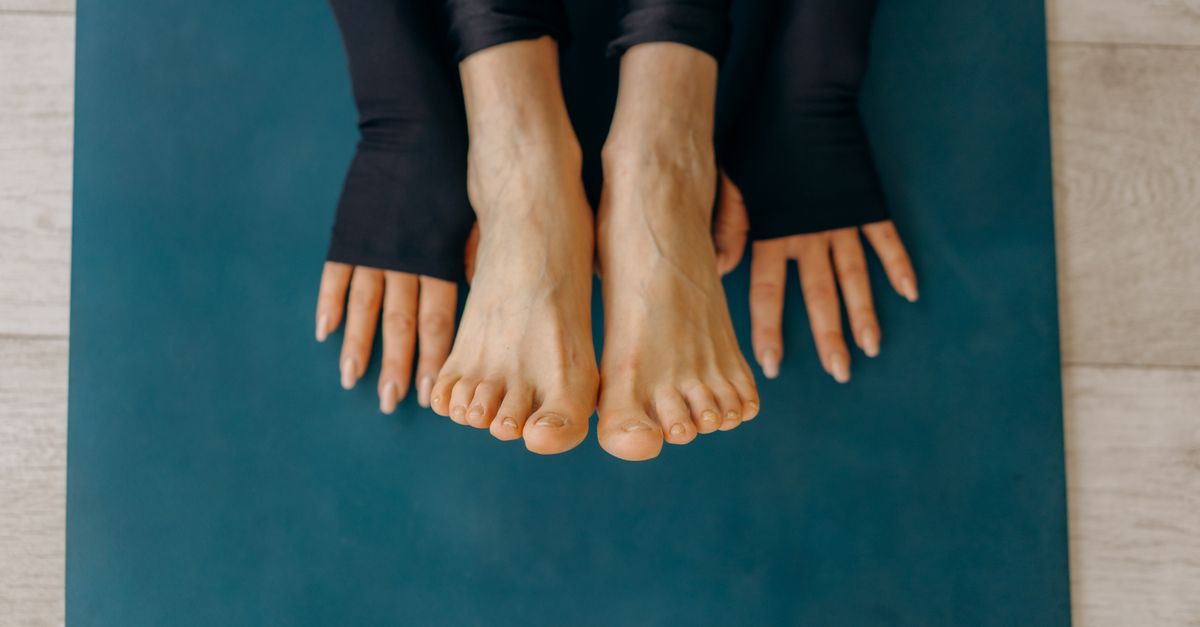 Close-up of feet and hands on a blue yoga mat in a calm indoor setting.