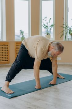 Elderly man practicing yoga on mat indoors, demonstrating fitness and health.