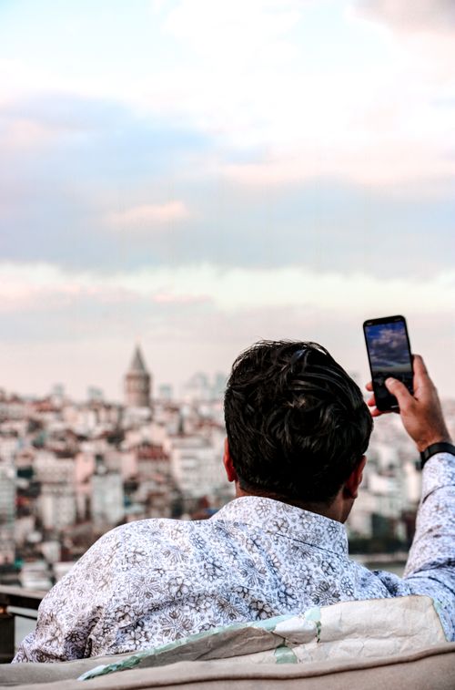Free A man captures the Istanbul skyline with his smartphone, featuring the Galata Tower under a cloudy sky. Stock Photo