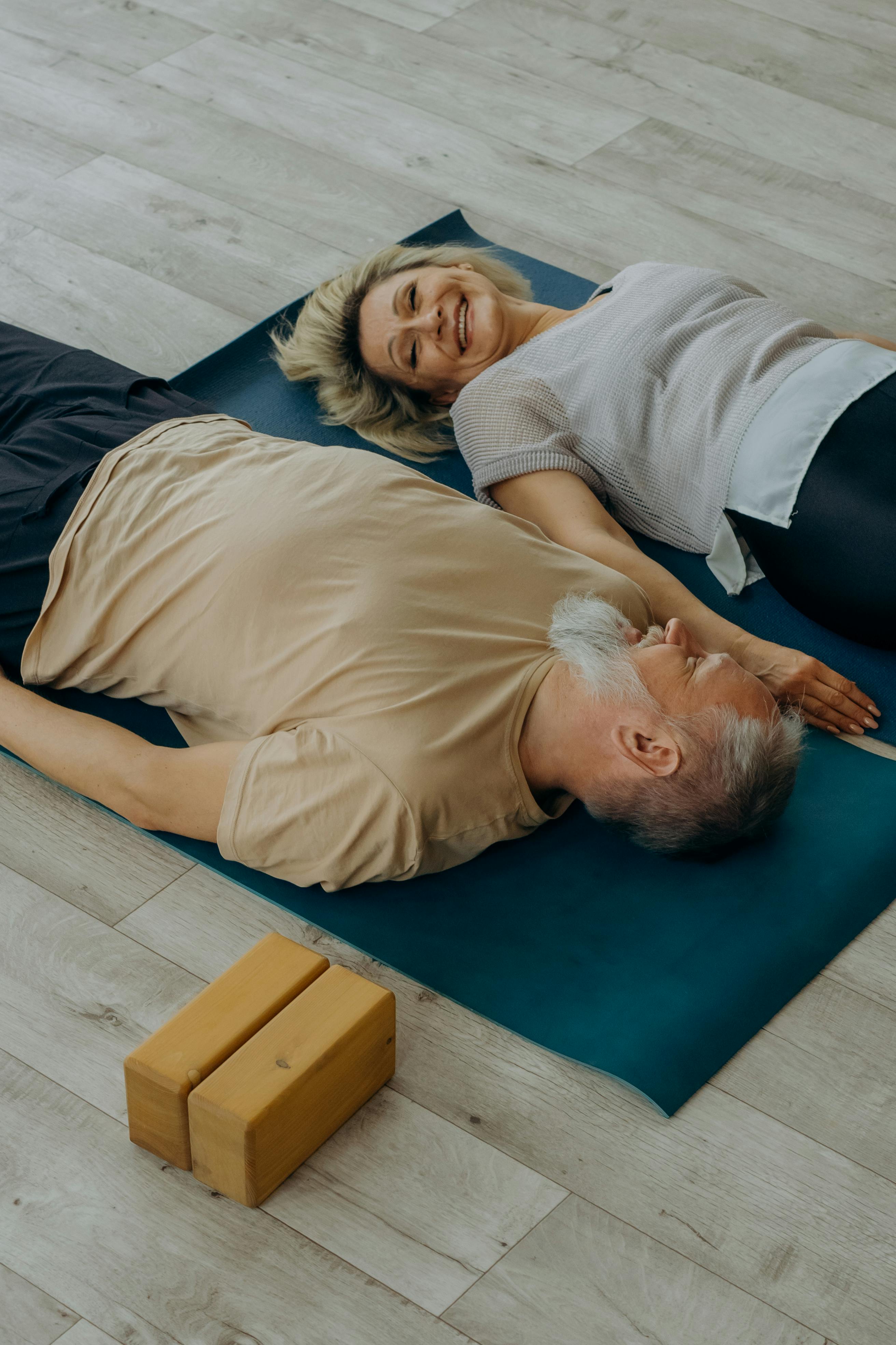 man in beige shirt lying on blue mat beside woman in gray shirt