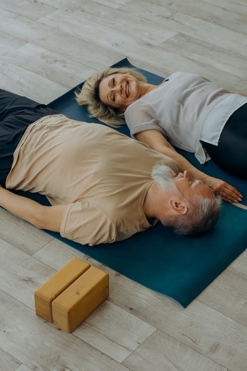 Man in Beige Shirt Lying on Blue Mat Beside Woman in Gray Shirt