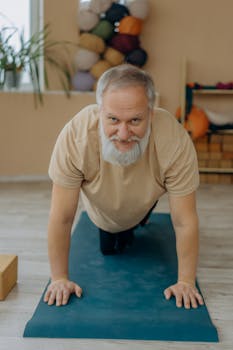 Elderly man with white hair exercising on a yoga mat indoors, promoting fitness and wellness.