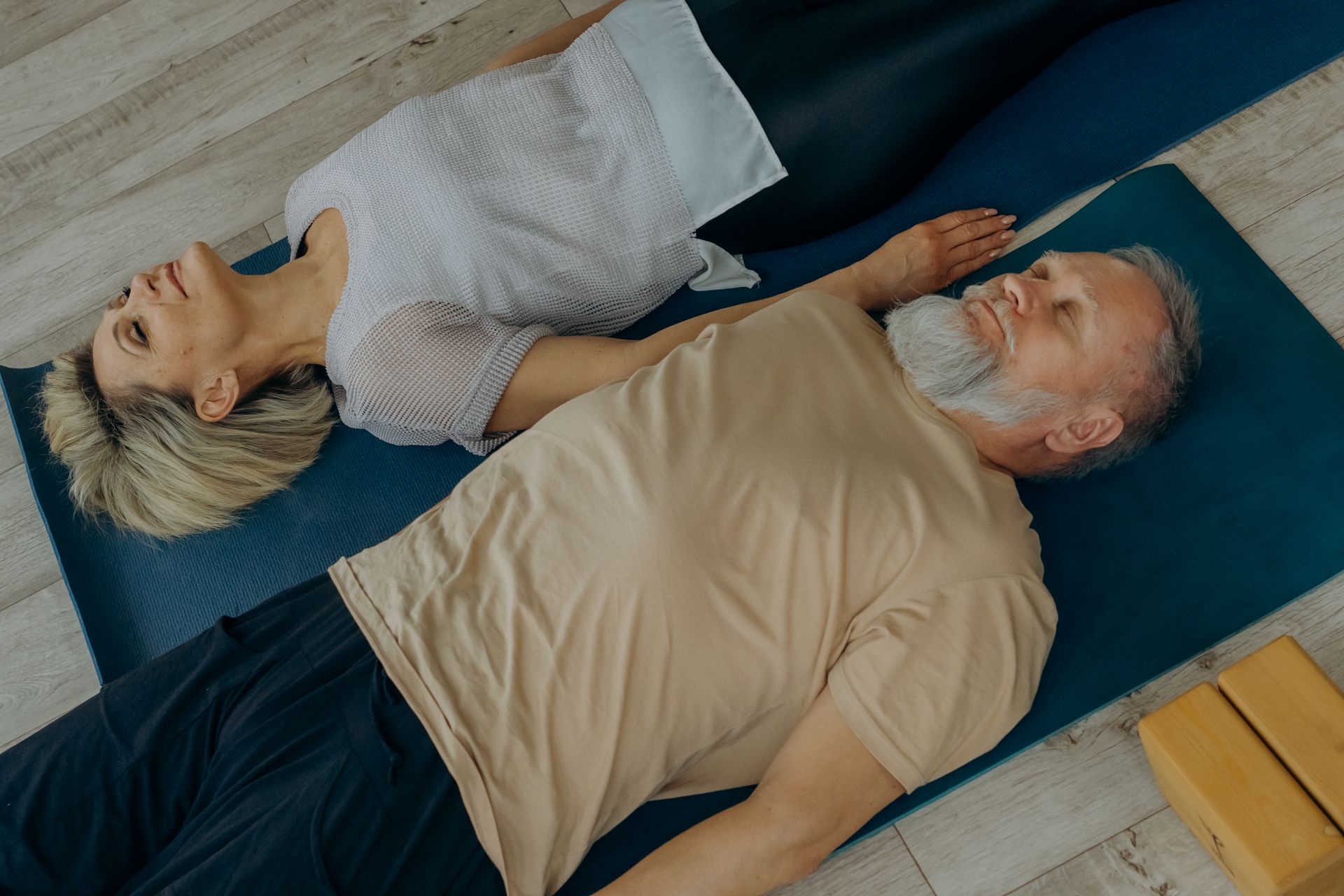 Man in Beige Shirt Lying on Blue Mat Beside Woman in Gray Shirt