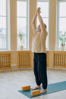 A senior man performs a yoga stretch indoors with blocks on a mat, promoting healthy lifestyle.