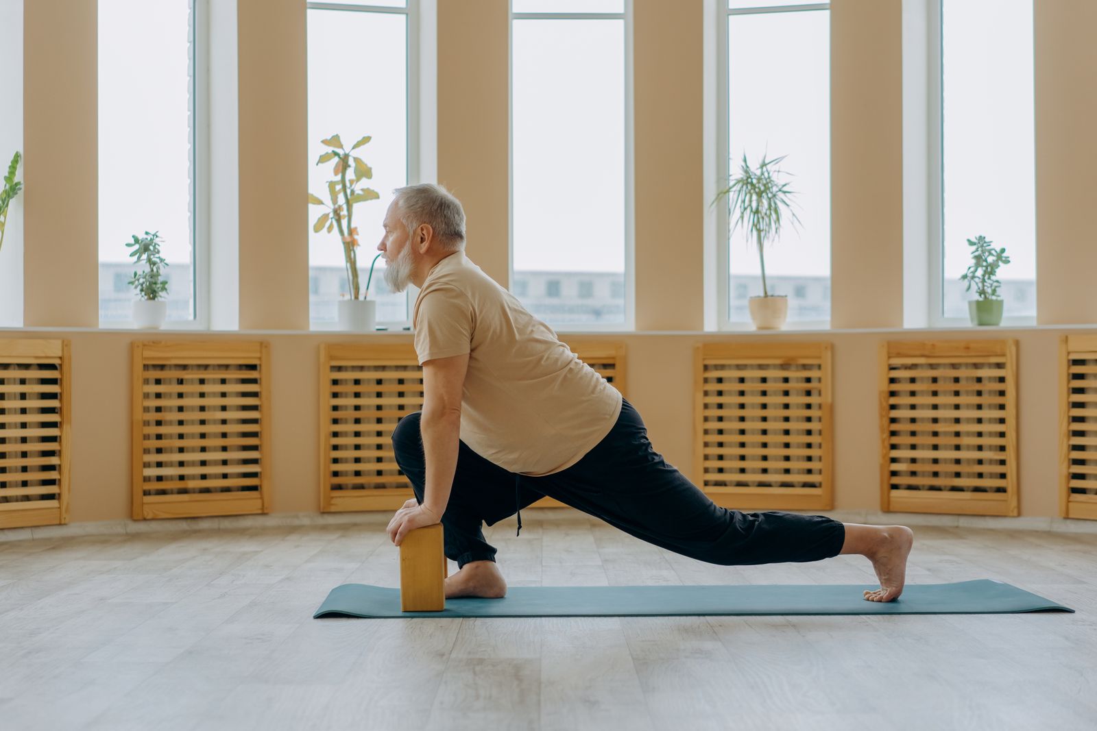 Older adult using a yoga block for support while stretching, reflecting Iyengar yoga's therapeutic approach