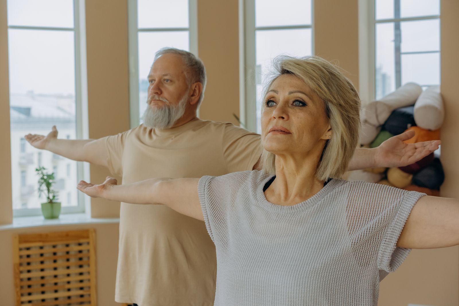 Elderly couple practicing gentle yoga with arms outstretched in a bright indoor space