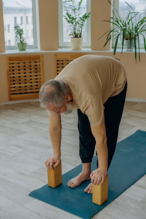 A Man in Brown T-shirt and Black Pants Bending Forward Pressing on Yoga Blocks