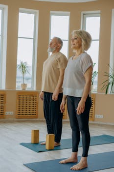Senior couple in activewear doing yoga together on mats indoors, embracing a healthy lifestyle.