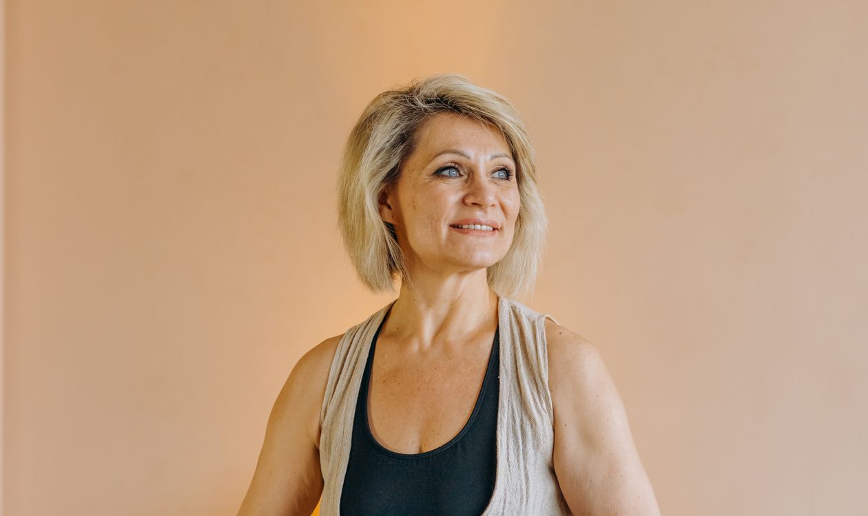 Older woman sitting calmly on a yoga mat at home, ready to stretch