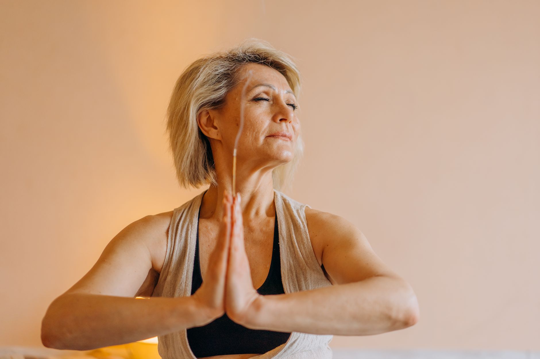 A senior woman meditating indoors with eyes closed, showcasing mental tranquility.
