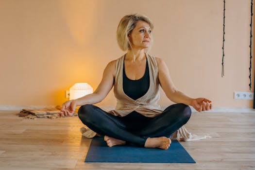A senior woman sits in a yoga pose indoors, promoting mindfulness and healthy living.