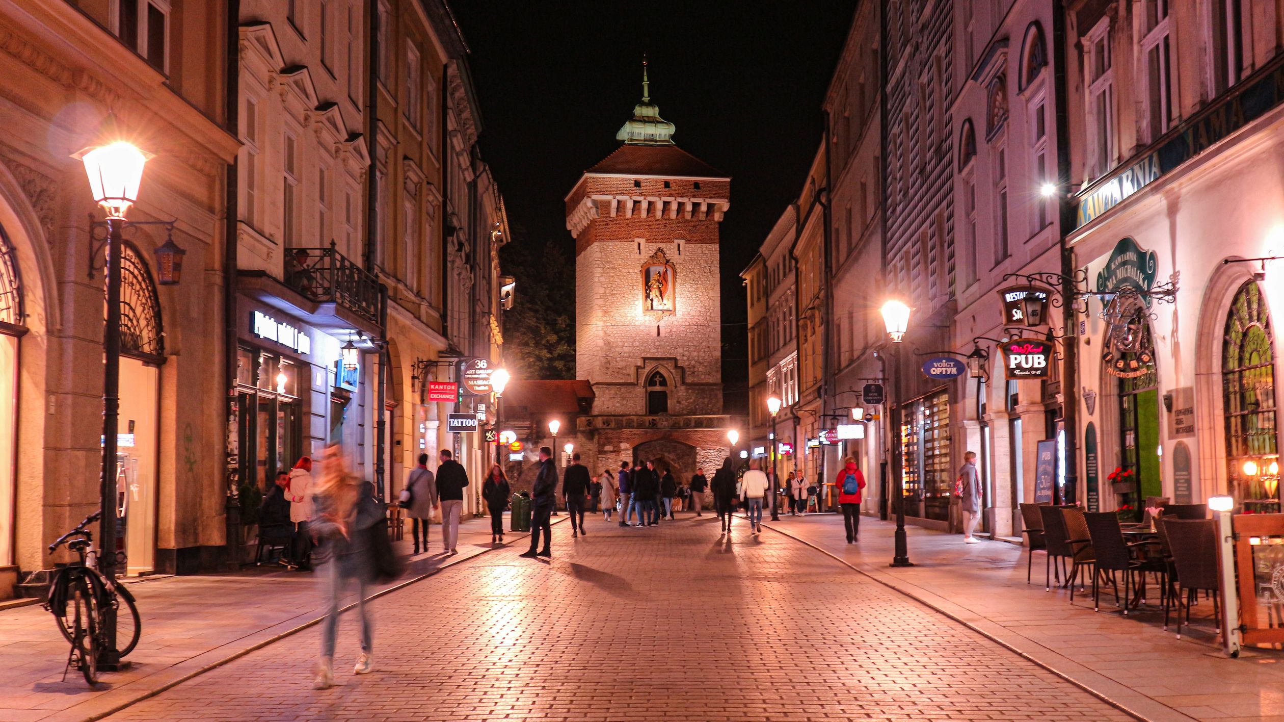 Vibrant night street scene in Krakow with St. Florian's Gate and lively pedestrian traffic.