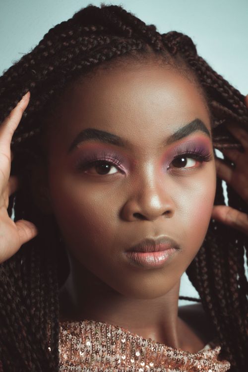 Free Close-up portrait of a woman with braided hair, showcasing vibrant makeup and elegant poise. Stock Photo