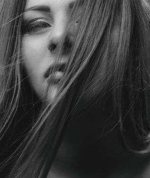 Close-up monochrome portrait capturing an expressive gaze through the hair.