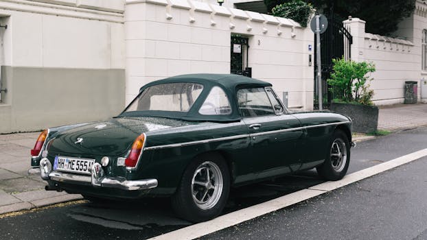 A classic vintage convertible car parked on a wet street in an urban area.