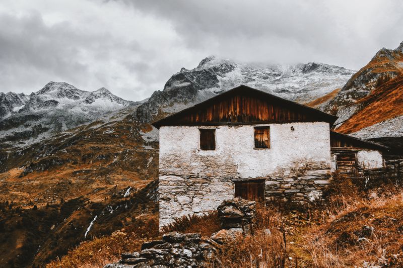 Scenic view of an abandoned cabin against snow-capped mountains in fall.