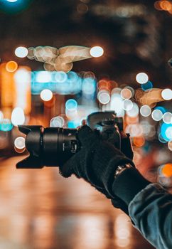 Person holding DSLR camera with gloves capturing bokeh city lights at night.